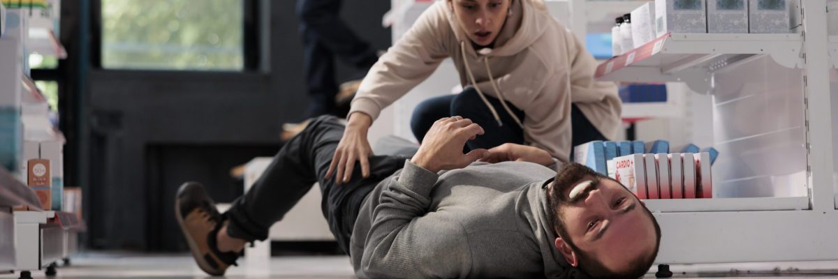 Terrified woman noticing man on drugstore floor having epileptic seizure, running to give first aid for fainting. Apothecary client helping person suffering from epilepsy disorder attack