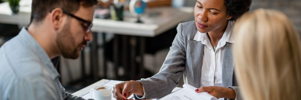 Black female real estate agent showing to a couple where to sign the contract during the meeting in the office.
