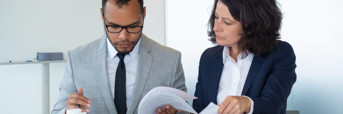 Business colleagues checking agreement text. Business man and woman sitting at meeting table and reading documents together. Teamwork concept