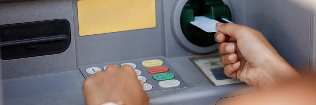 Close-up of woman typing pin code while withdrawing money from ATM.