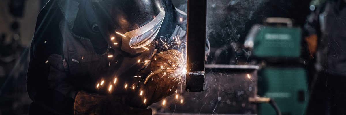 Man is working at metal factory, he is welding a piece of rail using special tools.