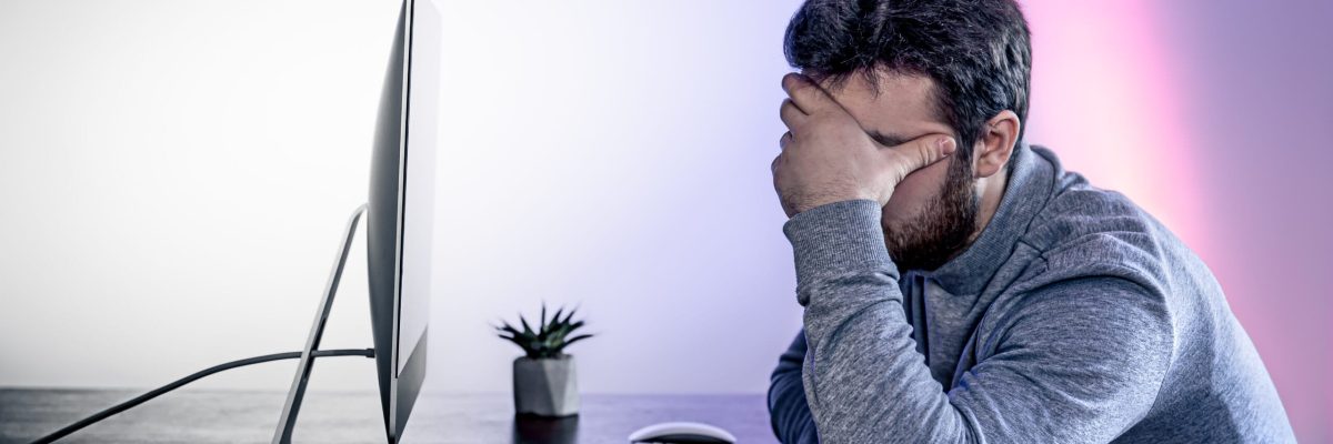 Tired man sits in front of the computer, covered his face with his hands, office work, night work, burnout at work.